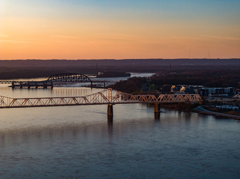 Aerial view of steel truss bridges spanning the Ohio River under a vibrant sunset sky with distant city silhouettes Louisville Kentucky United States. Aerial view of steel truss bridges spanning the Ohio River under a vibrant sunset sky with distant city silhouettes Louisville Kentucky United States.