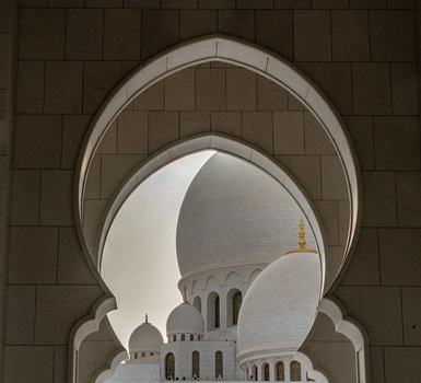 View of the white marble domes and intricate arches of a grand mosque framed by a stone archway in Abu Dhabi Abu Dhabi United Arab Emirates. View of the white marble domes and intricate arches of a grand mosque framed by a stone archway in Abu Dhabi Abu Dhabi United Arab Emirates.