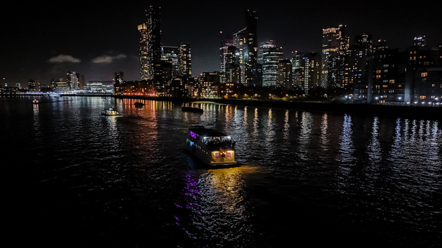 Aerial view of a boat cruising on the River Thames at night with the illuminated London skyline in the background London England United Kingdom.
