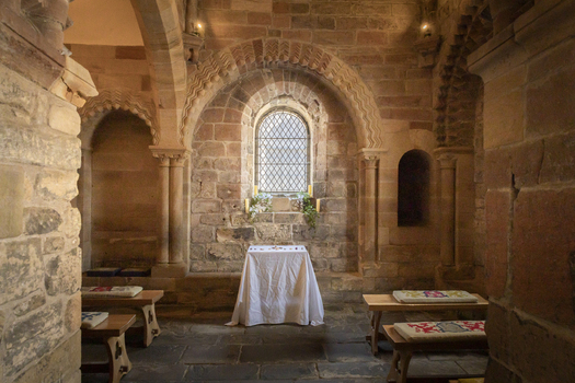 View of the historic stone chapel interior featuring arched windows a simple altar with a white cloth and wooden benches in the Castle Keep in Newcastle upon Tyne England United Kingdom. View of the historic stone chapel interior featuring arched windows a simple altar with a white cloth and wooden benches in the Castle Keep in Newcastle upon Tyne England United Kingdom.