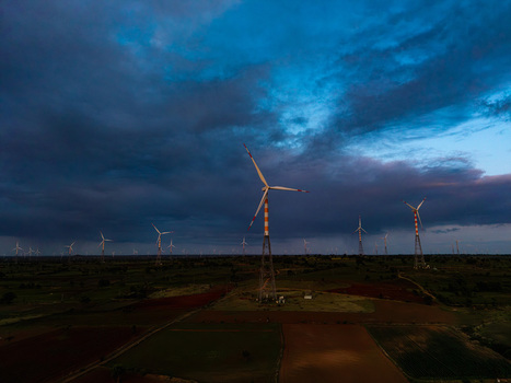 Aerial view of wind turbines standing in a rural landscape with agricultural fields under a dramatic stormy sky in Hampi Karnataka India.