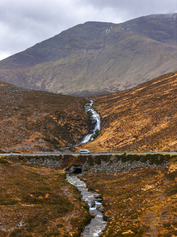 Aerial view of Eas a Bhradain waterfall cascading down a rugged hillside towards a road with a parked van in Isle of Skye Scotland United Kingdom. Aerial view of Eas a Bhradain waterfall cascading down a rugged hillside towards a road with a parked van in Isle of Skye Scotland United Kingdom.