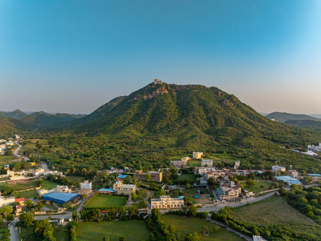 Aerial view of the Sajjangarh Monsoon Palace perched atop a lush green hill overlooking the residential landscape and surrounding terrain of Udaipur Rajasthan India.