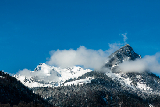 View of snow capped mountains piercing the vibrant blue sky partially veiled by soft fluffy clouds creating a serene yet majestic panorama Train from Lucerne Switzerland. View of snow capped mountains piercing the vibrant blue sky partially veiled by soft fluffy clouds creating a serene yet majestic panorama Train from Lucerne Switzerland.