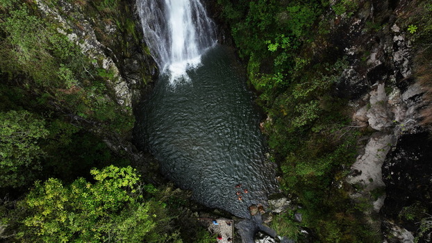 Aerial view of Salto de Aguas Blancas waterfall cascading into a deep pool surrounded by lush forest and rocky cliffs with people swimming in Constanza La Vega Province Dominican Republic. Aerial view of Salto de Aguas Blancas waterfall cascading into a deep pool surrounded by lush forest and rocky cliffs with people swimming in Constanza La Vega Province Dominican Republic.
