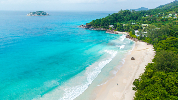 Aerial view of the pristine white sand beach and turquoise waters of Grand Anse Mahe surrounded by lush tropical vegetation and rocky coastline in Grand Anse Mahe Seychelles. Aerial view of the pristine white sand beach and turquoise waters of Grand Anse Mahe surrounded by lush tropical vegetation and rocky coastline in Grand Anse Mahe Seychelles.