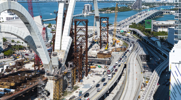 Aerial view of an elevated highway under construction for the Fountain Signature Bridge with ongoing traffic flowing underneath set against the backdrop of Biscayne Bay Miami Florida USA. Aerial view of an elevated highway under construction for the Fountain Signature Bridge with ongoing traffic flowing underneath set against the backdrop of Biscayne Bay Miami Florida USA.