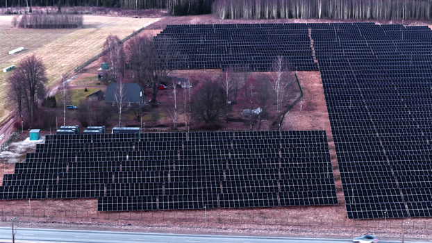 Aerial view of a large solar farm with rows of photovoltaic panels a small house surrounded by trees and a road in the foreground in Latvija. Aerial view of a large solar farm with rows of photovoltaic panels a small house surrounded by trees and a road in the foreground in Latvija.