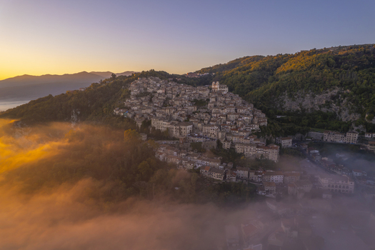 Aerial view of the historic hilltop town of Artena surrounded by golden mist and lush hills at sunset in Artena Lazio Italy.