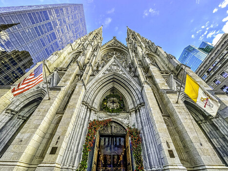 New York United States 28 November 2022 View of the neo Gothic facade of St. Patrick s Cathedral on Fifth Avenue decorated with holiday wreaths and flags under a blue sky.