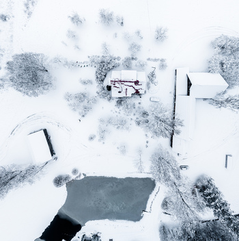 Aerial view of a snow covered landscape featuring farm buildings and a frozen pond surrounded by trees in Latvia. Aerial view of a snow covered landscape featuring farm buildings and a frozen pond surrounded by trees in Latvia.
