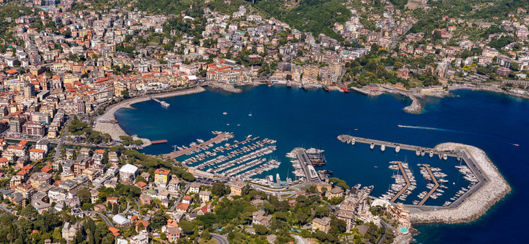 Aerial view of the harbor and coastal town of Rapallo with colorful buildings yachts moored in the marina and lush green hills under bright sunlight in Rapallo Liguria Italy. Aerial view of the harbor and coastal town of Rapallo with colorful buildings yachts moored in the marina and lush green hills under bright sunlight in Rapallo Liguria Italy.