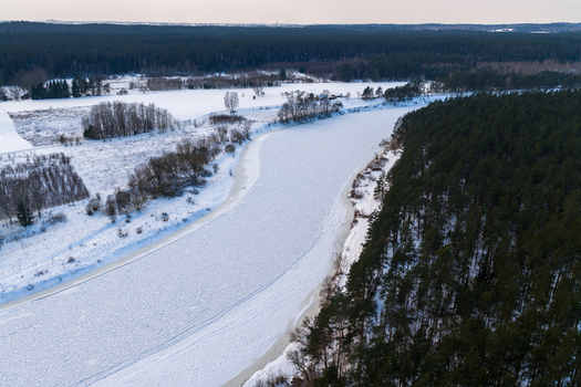 Aerial view of a frozen river winding through a snowy winter landscape and dense evergreen forests under an overcast sky Lithuania. Aerial view of a frozen river winding through a snowy winter landscape and dense evergreen forests under an overcast sky Lithuania.