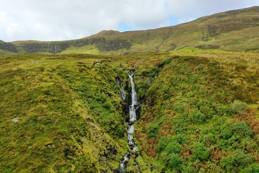 Aerial view of Bride s Veil Falls cascading down a lush green hillside near Portree Scotland United Kingdom. Aerial view of Bride s Veil Falls cascading down a lush green hillside near Portree Scotland United Kingdom.