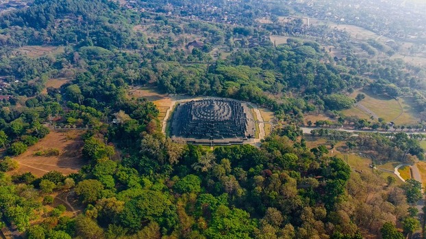 Aerial view of Borobudur Temple surrounded by lush green trees and tropical vegetation in Kecamatan Borobudur Jawa Tengah Indonesia.