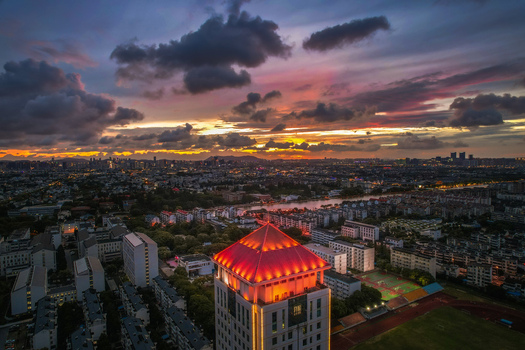Aerial view of the illuminated red roof of Suzhou University Qian Bldg. No.5 overlooking the urban skyline under a dramatic sunset sky in Suzhou Jiangsu China.