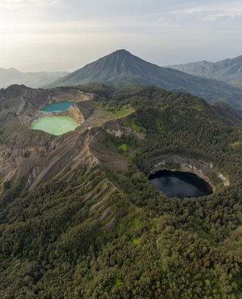 Aerial view of Kelimutu National Park with its iconic turquoise green and black volcanic crater lakes surrounded by lush forest and mountains Detusoko East Nusa Tenggara Indonesia.