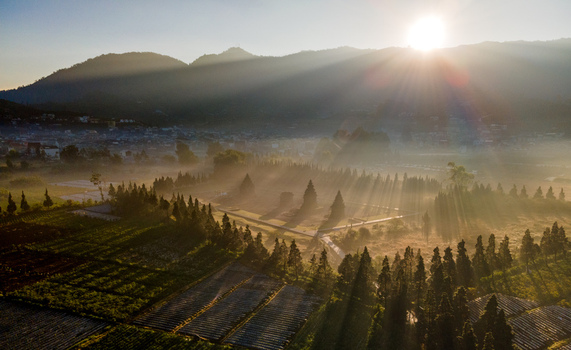 Aerial view of Dieng Plateau at sunrise featuring ancient temples misty pine trees and agricultural fields with dramatic sun rays in Kecamatan Batur Jawa Tengah Indonesia. Aerial view of Dieng Plateau at sunrise featuring ancient temples misty pine trees and agricultural fields with dramatic sun rays in Kecamatan Batur Jawa Tengah Indonesia.