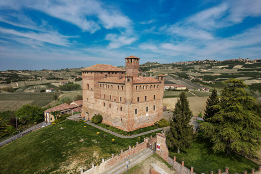 Aerial view of the medieval Grinzane Cavour Castle surrounded by rolling vineyards and lush green hills under a blue sky Grinzane Cavour Piedmont Italy. Aerial view of the medieval Grinzane Cavour Castle surrounded by rolling vineyards and lush green hills under a blue sky Grinzane Cavour Piedmont Italy.