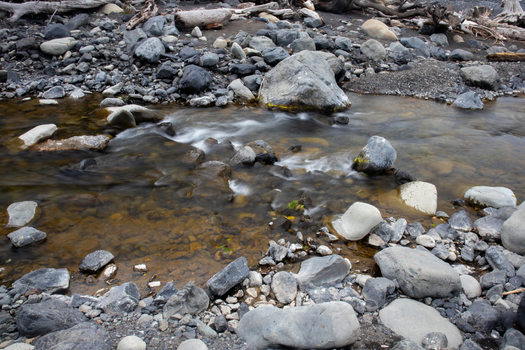 View of a clear stream flowing over smooth grey stones and pebbles along the rugged shoreline of the Lost Coast in Humboldt County California United States.