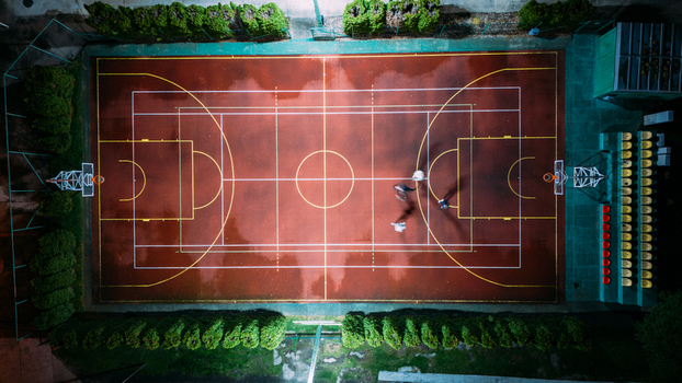 Aerial view of the illuminated basketball court the red and brown ground contrasts with the white lines and the green trees Sremska Mitrovica Vojvodina Serbia. Aerial view of the illuminated basketball court the red and brown ground contrasts with the white lines and the green trees Sremska Mitrovica Vojvodina Serbia.