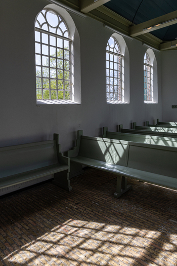 View of the interior of the historic Enkhuizerkerk church with wooden pews and arched windows casting shadows on the brick floor in Schokland Flevoland Netherlands.