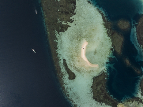 Aerial view of a small sandbar surrounded by turquoise coral reefs and deep blue ocean near Flores East Nusa Tenggara Indonesia.