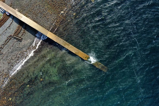 Aerial view of a concrete pier extending into the dark blue sea with a rocky shoreline and clear water Stein Scotland United Kingdom. Aerial view of a concrete pier extending into the dark blue sea with a rocky shoreline and clear water Stein Scotland United Kingdom.