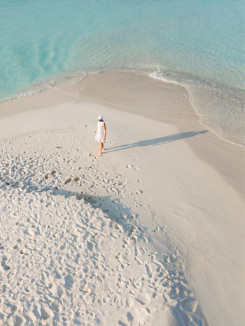 Aerial view of a solitary figure in white attire walking along the sandy shores where turquoise waters meet creating a tranquil scene Dhidhdhoo Maldives.