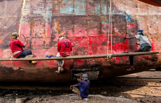 Dhaka Bangladesh 20 April 2026 View of dedicated workers meticulously tending to the vast rust streaked hull of a ship its vibrant red and muted brown tones contrasting with the gritty ground.