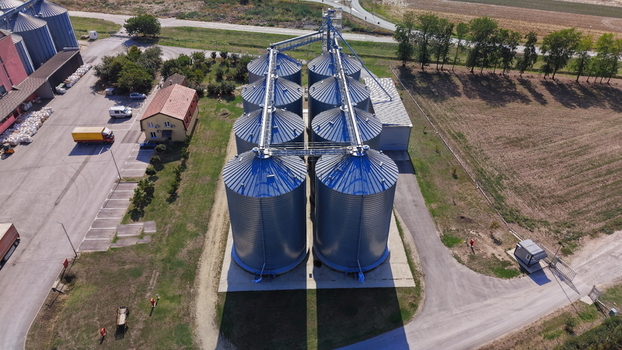 Aerial view of the storage silo Bavaniste facility featuring metallic cylindrical grain silos with blue roofs surrounded by rural landscape and fields in Bavaniste Vojvodina Serbia.