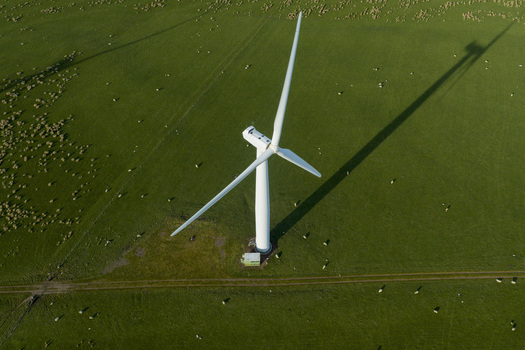 Aerial view of a large white wind turbine casting a long shadow over a green field with grazing sheep in Scotland United Kingdom. Aerial view of a large white wind turbine casting a long shadow over a green field with grazing sheep in Scotland United Kingdom.