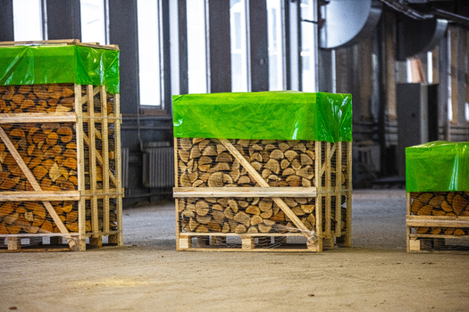 View of stacked firewood in wooden crates covered with green plastic sheets inside a warehouse in Latvia. View of stacked firewood in wooden crates covered with green plastic sheets inside a warehouse in Latvia.