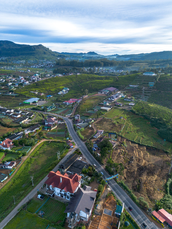 Aerial view of the town of Nuwara Eliya featuring lush tea plantations rolling hills a winding road and residential buildings in Nuwara Eliya Central Province Sri Lanka. Aerial view of the town of Nuwara Eliya featuring lush tea plantations rolling hills a winding road and residential buildings in Nuwara Eliya Central Province Sri Lanka.