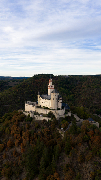 Aerial view of Marksburg castle perched on a hilltop surrounded by dense forest and rolling hills in Braubach Rhineland Palatinate Germany. Aerial view of Marksburg castle perched on a hilltop surrounded by dense forest and rolling hills in Braubach Rhineland Palatinate Germany.