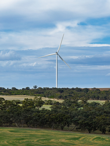 Aerial view of a wind turbine standing in a rural landscape with green fields and native trees under a cloudy blue sky in Nhill Victoria Australia. Aerial view of a wind turbine standing in a rural landscape with green fields and native trees under a cloudy blue sky in Nhill Victoria Australia.