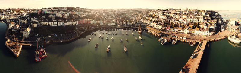 Aerial view of the harbor featuring colorful houses on the hillside and numerous fishing boats moored in the calm water Brixham England United Kingdom.