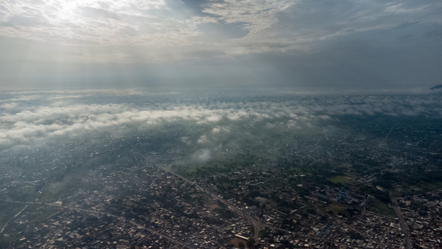 Aerial view of the city of Ho nestled in the Volta Region featuring dense urban rooftops partially obscured by a low hanging layer of morning mist under a bright sky Ho Volta Region Ghana. Aerial view of the city of Ho nestled in the Volta Region featuring dense urban rooftops partially obscured by a low hanging layer of morning mist under a bright sky Ho Volta Region Ghana.