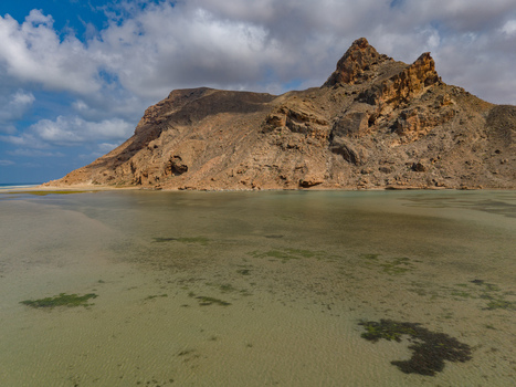 Aerial view of the stark rocky mountain rising majestically from the tranquil shallow waters of the lagoon its slopes meeting the clear patterned sea Detwah lagoon Socotra Yemen.