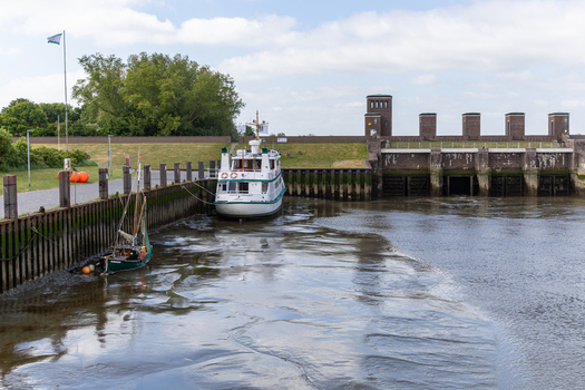 View of the Jantje von Dangast boat moored at the harbor lock during low tide with muddy ground and brick sluice gates Varel Lower Saxony Germany. View of the Jantje von Dangast boat moored at the harbor lock during low tide with muddy ground and brick sluice gates Varel Lower Saxony Germany.