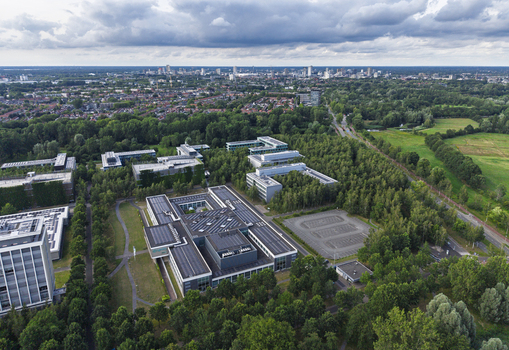 Aerial view of High Tech Campus Eindhoven featuring modern office buildings set among lush trees and a parking lot with the city skyline in Eindhoven Noord Brabant Netherlands. Aerial view of High Tech Campus Eindhoven featuring modern office buildings set among lush trees and a parking lot with the city skyline in Eindhoven Noord Brabant Netherlands.