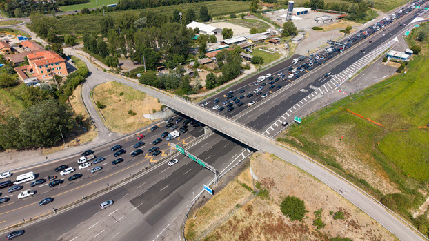 Aerial view of heavy traffic congestion on the A1 motorway with vehicles moving slowly across the highway infrastructure surrounded by green fields in Melegnano Lombardy Italy.