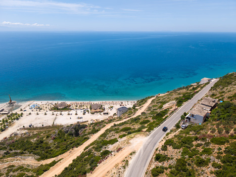 Aerial view of the turquoise waters of the Ionian Sea meeting the sandy shores of Borsh Beach with a winding coastal road on the hillside in Borsh Vlore County Albania. Aerial view of the turquoise waters of the Ionian Sea meeting the sandy shores of Borsh Beach with a winding coastal road on the hillside in Borsh Vlore County Albania.