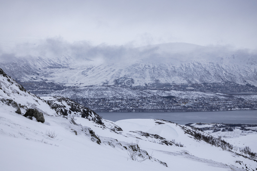 View of snow covered mountains and a calm fjord under a misty winter sky Kvaloya Troms Norway.