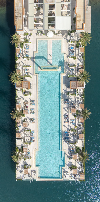 Aerial view of a long rectangular swimming pool at a luxury resort surrounded by sun loungers palm trees and clear blue water in Tivat Tivat Municipality Montenegro. Aerial view of a long rectangular swimming pool at a luxury resort surrounded by sun loungers palm trees and clear blue water in Tivat Tivat Municipality Montenegro.