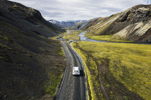 Aerial view of a white car driving on the F208 gravel road through a volcanic valley with a winding river and mossy hills in the Highlands of Iceland Iceland. Aerial view of a white car driving on the F208 gravel road through a volcanic valley with a winding river and mossy hills in the Highlands of Iceland Iceland.