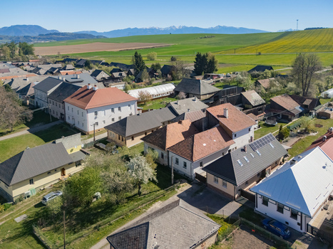 Aerial view of traditional houses with red rooftops and green gardens under a clear blue sky with mountains in the distance in Partizanska Lupca Zilina Region Slovakia.