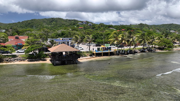 Aerial view of the coastal area in West End featuring a wooden pavilion a Roatan sign palm trees and a road with a gas station in West End Bay Islands Department Honduras.