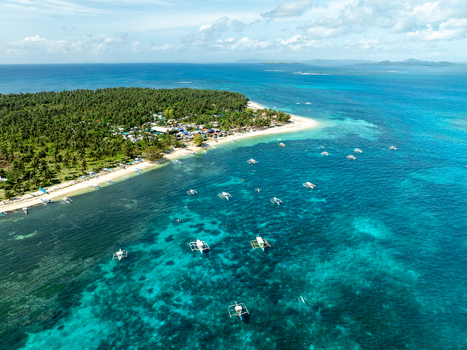 Aerial view of a lush tropical island with dense palm trees white sandy beaches and numerous outrigger boats floating in the clear turquoise waters of Siargao Philippines. Aerial view of a lush tropical island with dense palm trees white sandy beaches and numerous outrigger boats floating in the clear turquoise waters of Siargao Philippines.