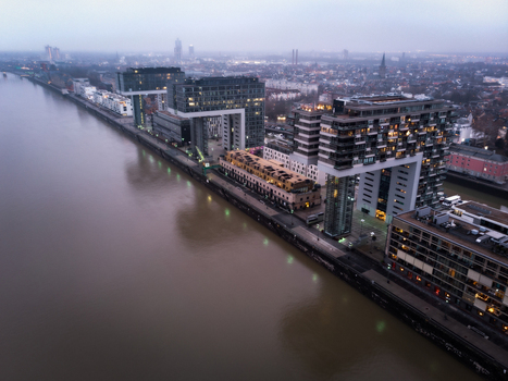 Aerial view of the modern Kranhaus buildings along the Rhine river at dusk with city lights and a hazy sky in Cologne North Rhine Westphalia Germany.